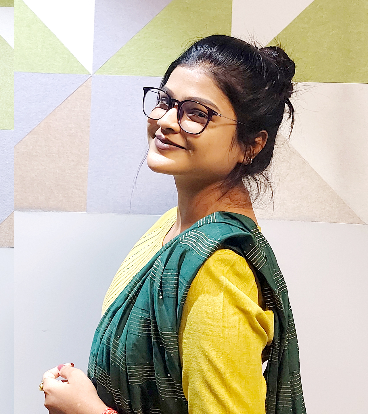A girl in spectacles and wearing green smiling at the camera.