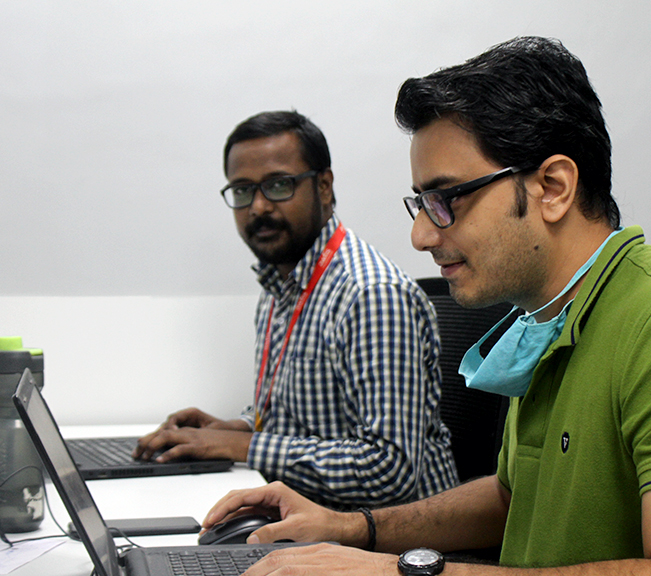 Two employees, one looking at the camera and another at the laptop, working at their desks