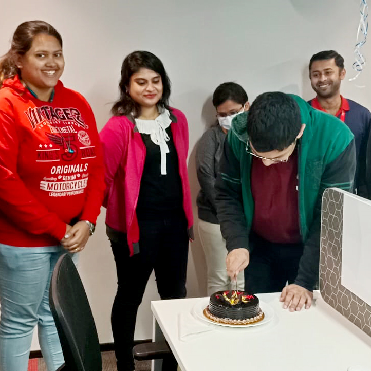 Person cutting cake with others standing around