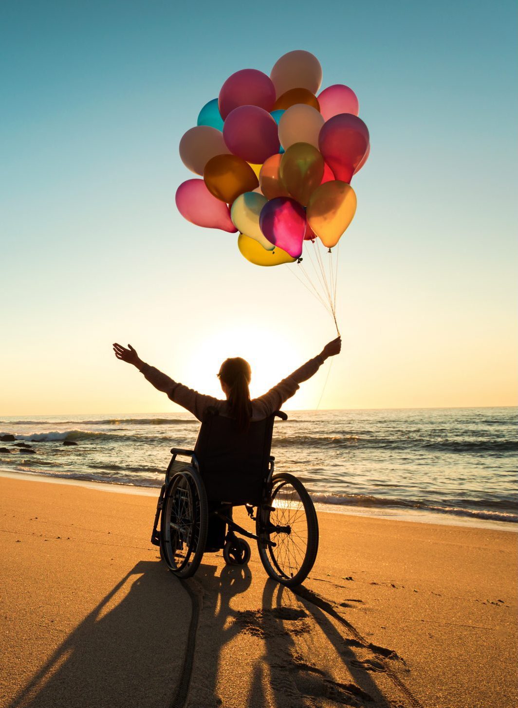 A woman in a wheelchair is holding some balloons at the sea beach