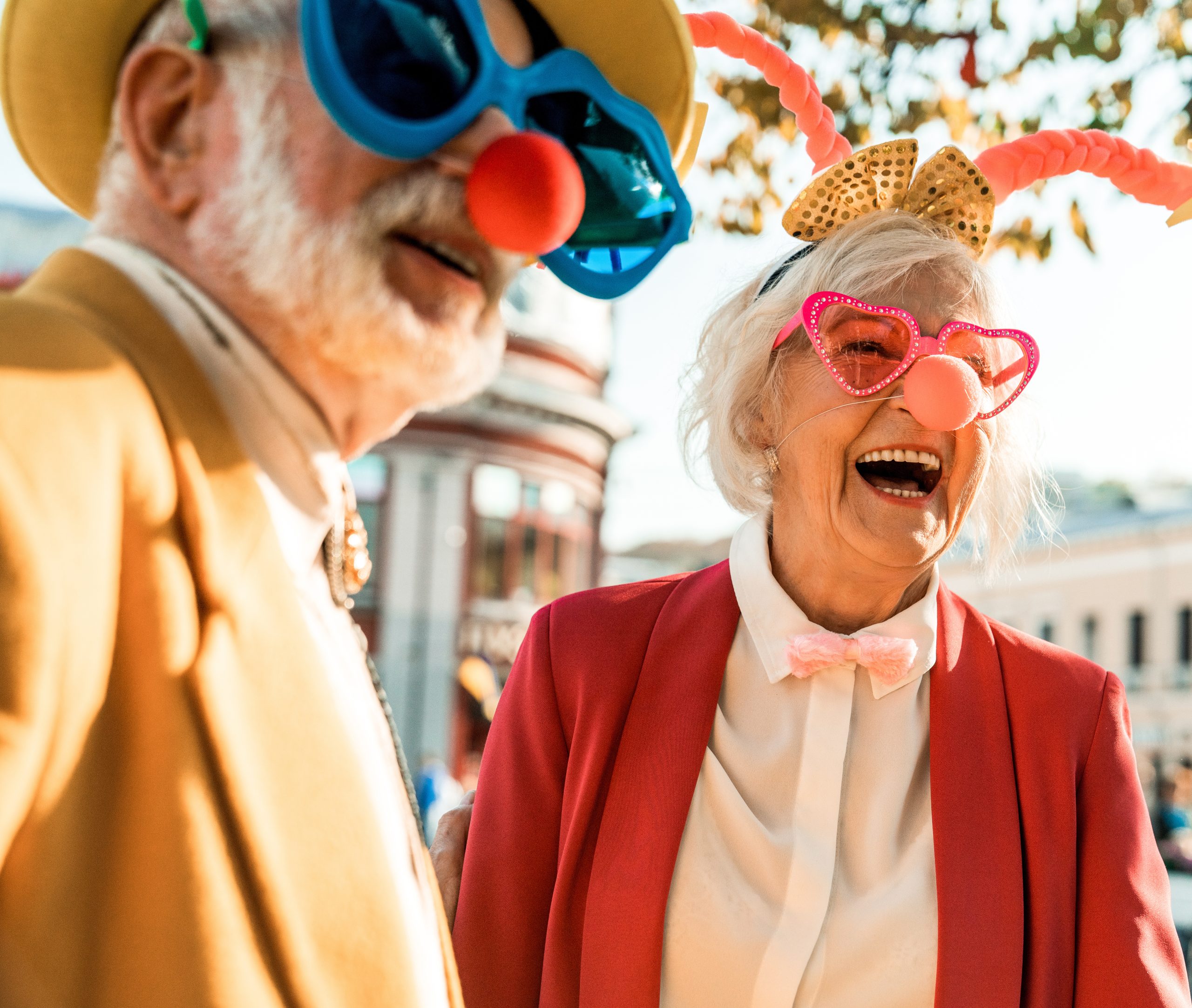An elderly couple is wearing oversized sunglasses and clown noses