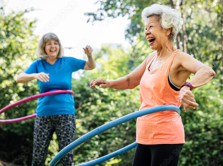 Two elderly women are hula hooping and smiling